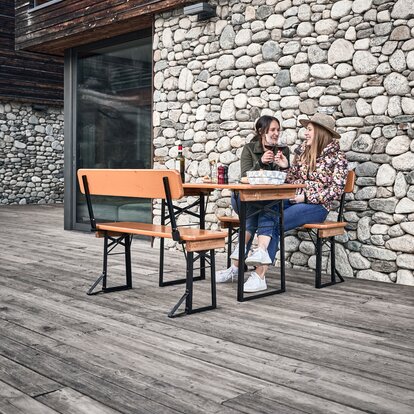 Two friends sit on the short beer tent set with backrest and clink glasses.