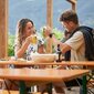 A couple clink two beer mugs together while sitting on classic beer tent sets.